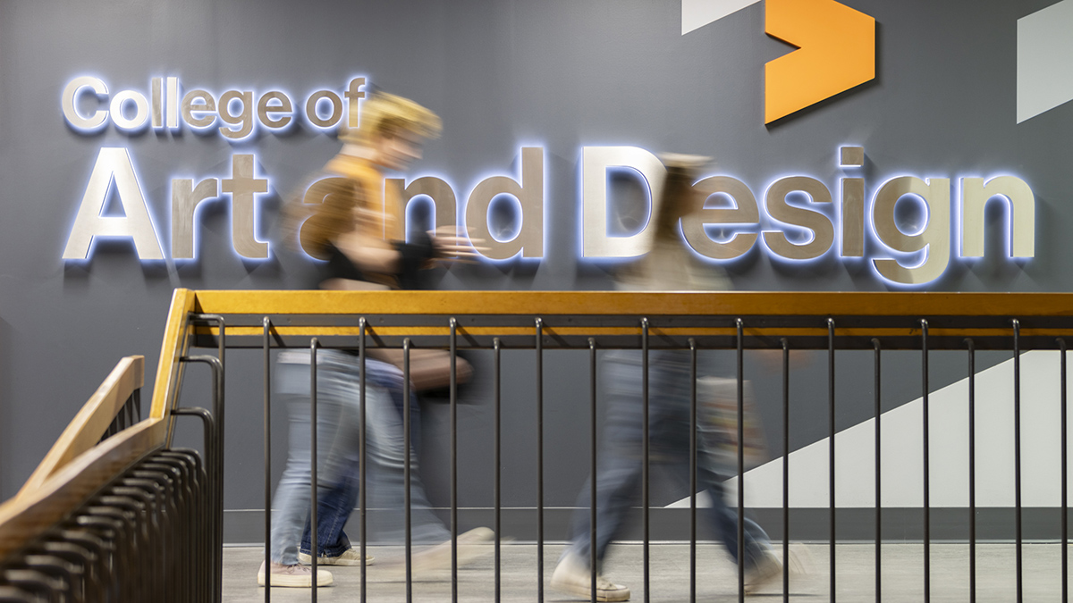 People walk in front of an LED College of Art and Design sign.