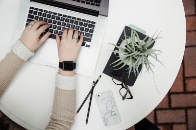 person typing on laptop at round table with plant, phone and glasses nearby