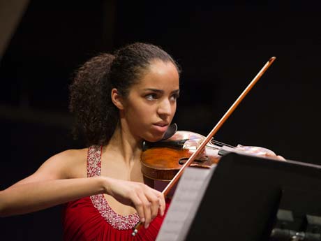 A violinist playing a piece of music with a dark backdrop 