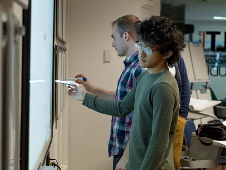 A student and professor working on a white board next to one another