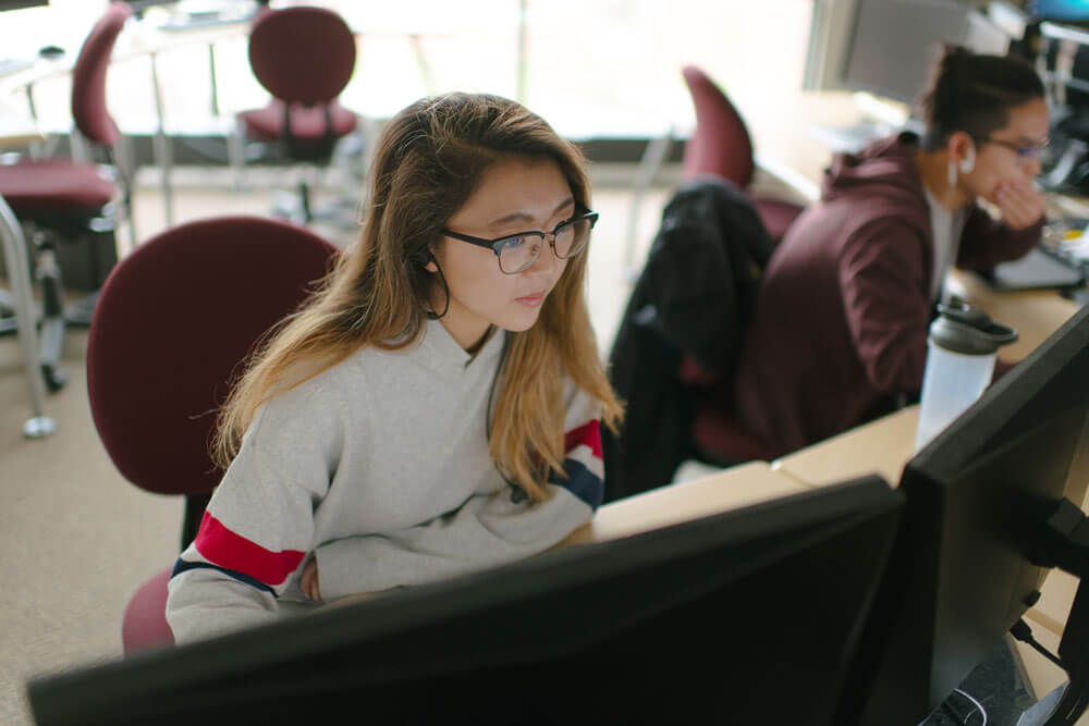 Two RIT students sitting at a desk and working on a computer.