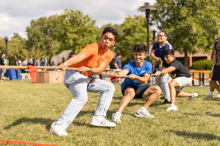 Three students pull on a rope during an outdoor game of tug-of-war.