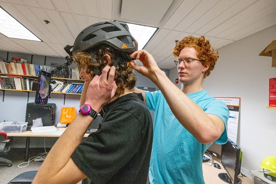 a student adjusts a helmet face camera for another student.