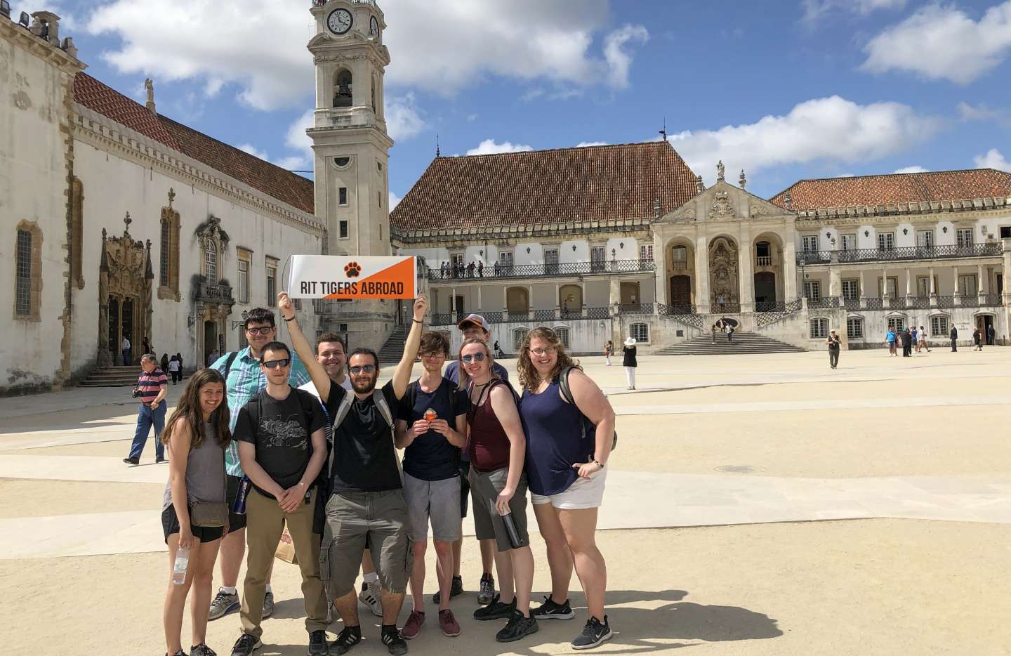 A group of students holds a "RIT Tigers Abroad" banner in front of a historic building with intricate architecture.