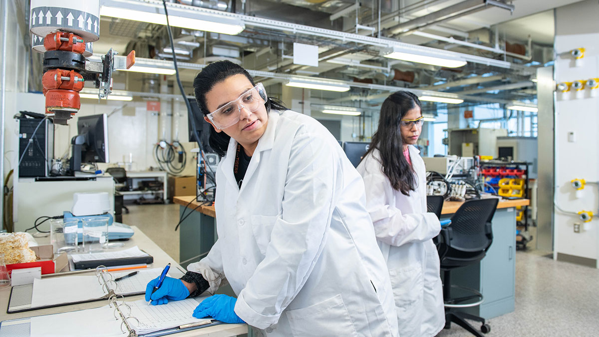 Two scientists in lab coats conducting research and taking notes in a high-tech laboratory.